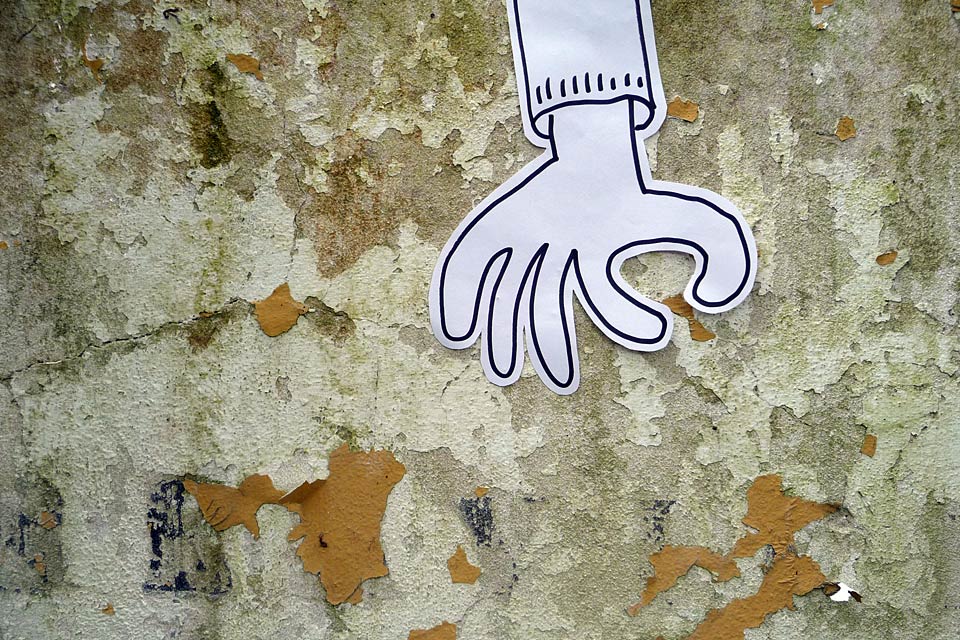 La mano, no más, junto a una pared desconchada